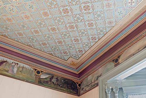 A corner view of Villa Alba’s dining room, with its painted frieze featuring scenes from Sir Walter Scott’s Rob Roy, and also showing a glimpse of  the room’s intricate stencilled and hand painted ceiling